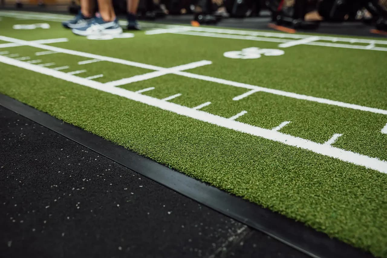 Primer plano de una pista sled verde Heroturfs con marcaje blanco en un gimnasio